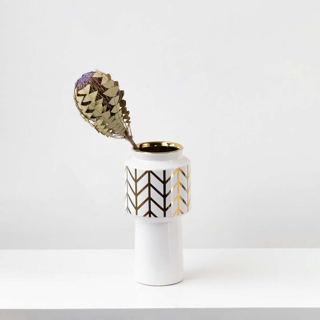 A tall white vase with gold patterned detailing shown in a minimal lifestyle setup creating a refined and modern look for home decor styling.