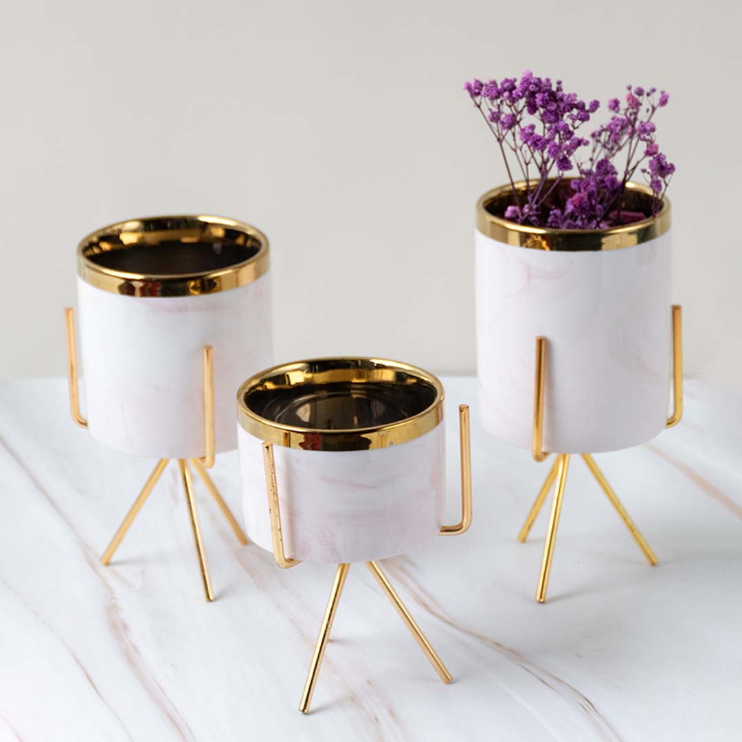 A stylish white marble planter with a gold stand arranged in a grouped lifestyle scene adding a refined modern accent to home decor settings.
