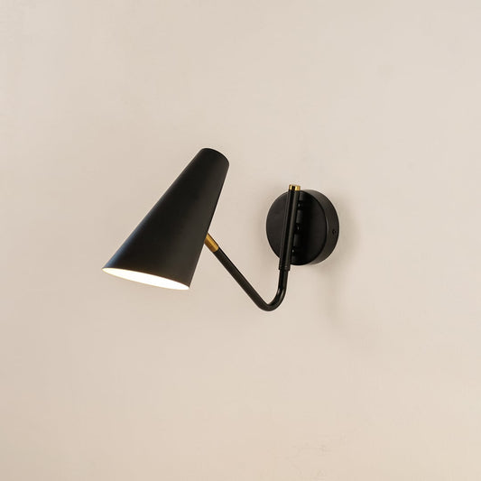 Black cone wall light with brass accents glowing softly on white wall offering modern elegance and ambient lighting style.