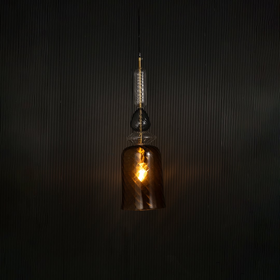 Elegant gold pendant light illuminated beautifully against dark background highlighting its glossy artistic texture.