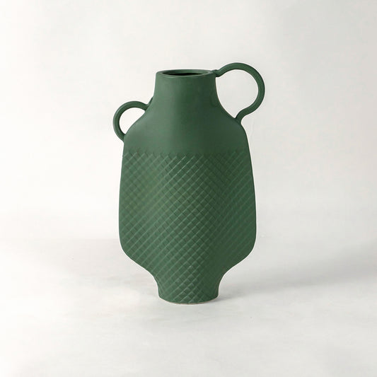 Green ceramic vase with dual side handles and textured surface placed on white surface against neutral background enhancing contemporary home decor aesthetic.