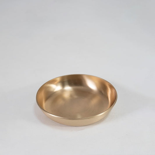 Single round brass bowl with smooth interior and matte gold finish placed centrally on white background surface.