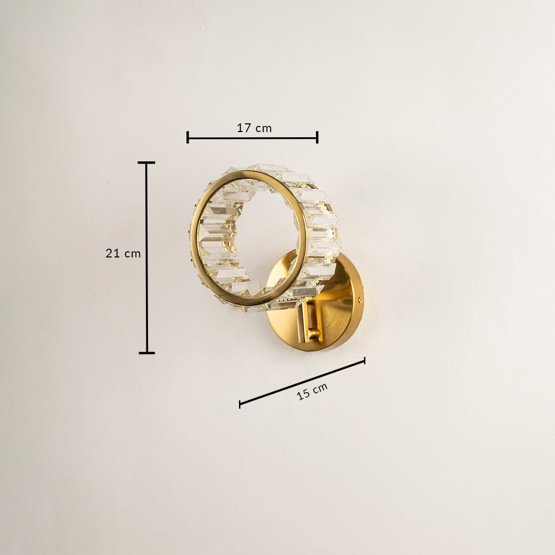 A glass and gold metal wall light with the light off mounted on a dark ribbed background showcasing its sculptural form and adding bold artistic contemporary décor.