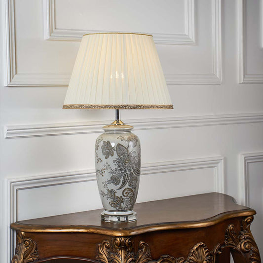 Grey floral ceramic table lamp with pleated fabric shade offering timeless traditional style and warm ambient lighting.