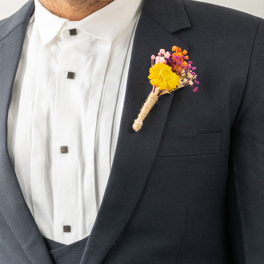 Detailed close up view of a yellow and orange dried flower boutonniere pinned to a luxury navy suit jacket lapel panel.