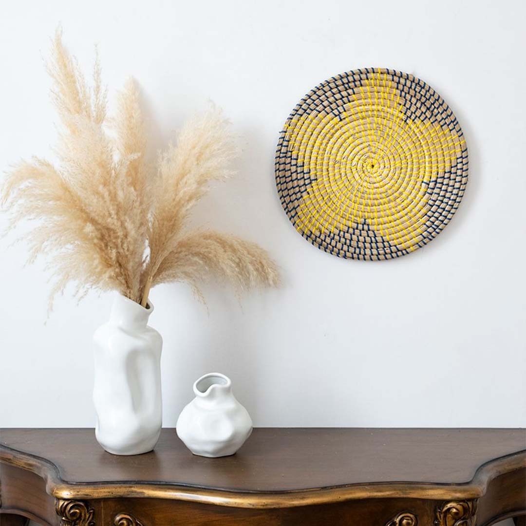 Handwoven wicker wall plate decor in yellow navy and beige star design styled on wall with boho home accessories.