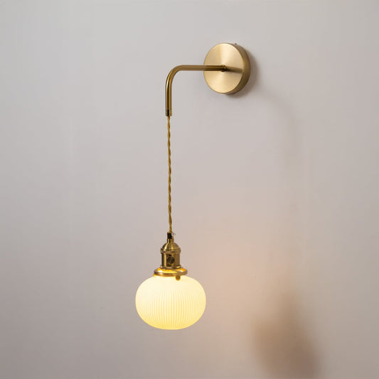 Gold metal wall light with white ribbed globe shade glowing softly on white background for elegant modern home decor.