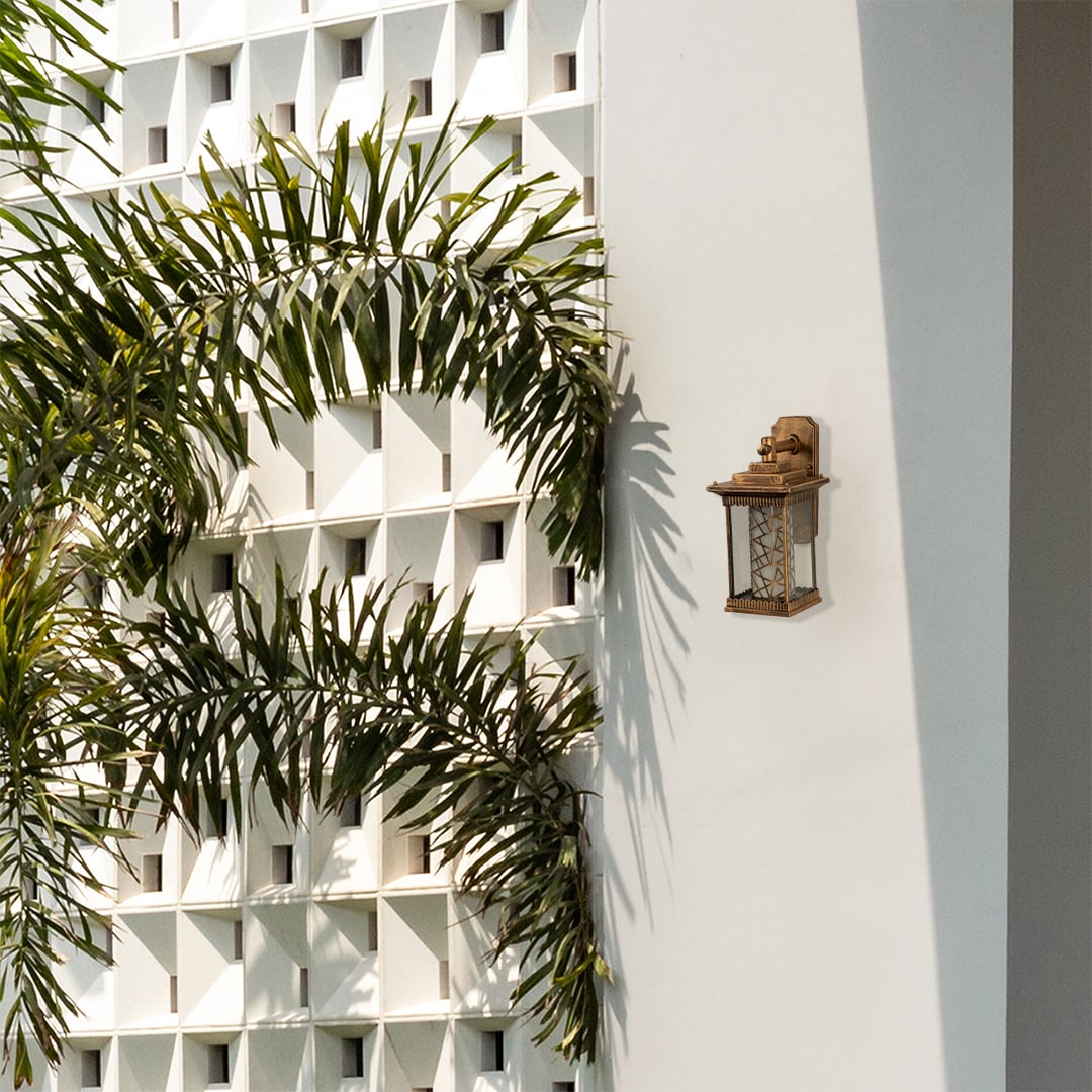 Gold metal outdoor wall lantern with patterned glass displayed on a modern white exterior wall with greenery adding refined outdoor decor styling.