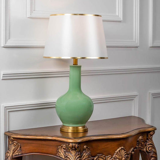 Table lamp with green ceramic base and white fabric shade on wooden console table classic elegant lighting for living room decor.