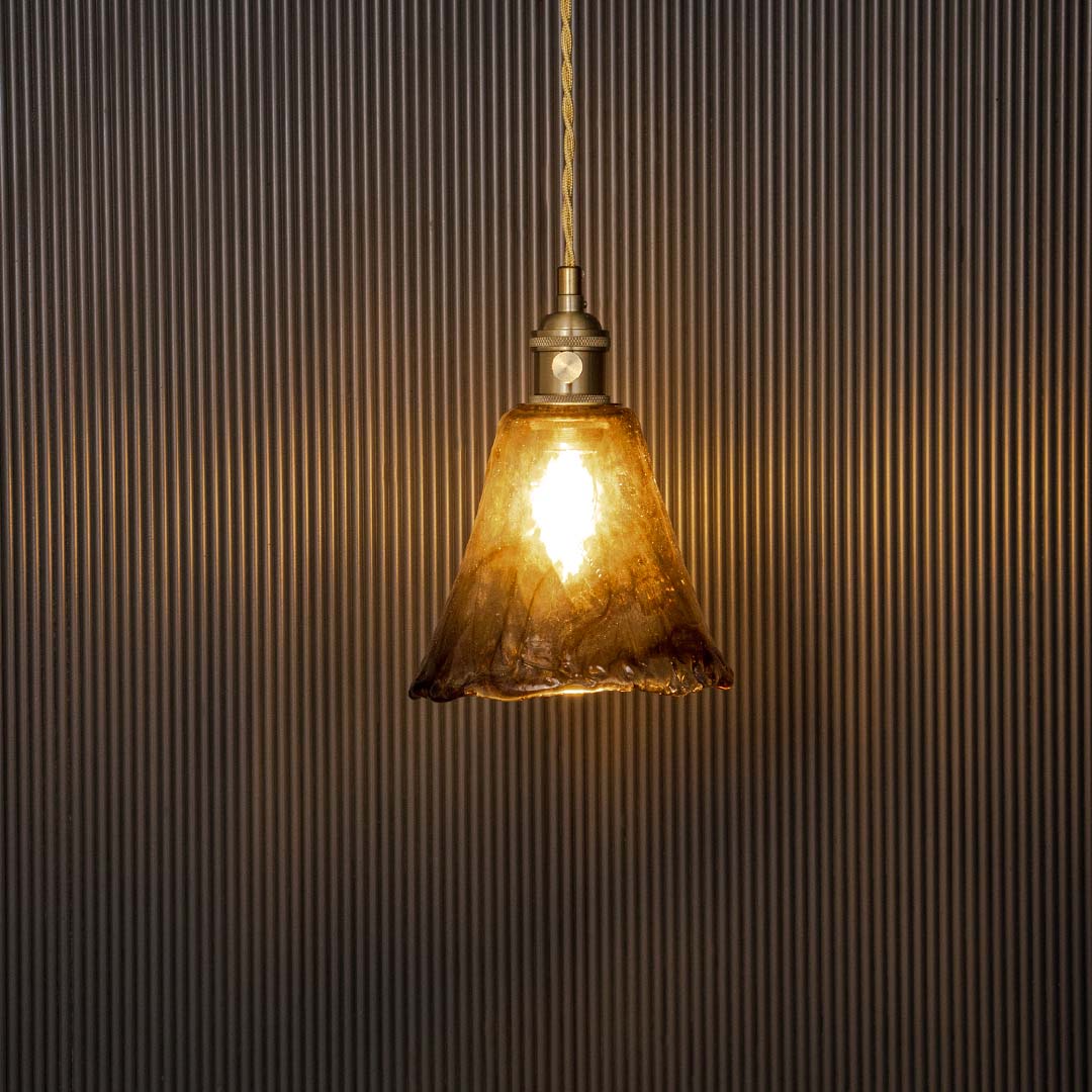Wavy amber glass pendant light glowing warmly on black background ideal for dining kitchen and living room lighting.