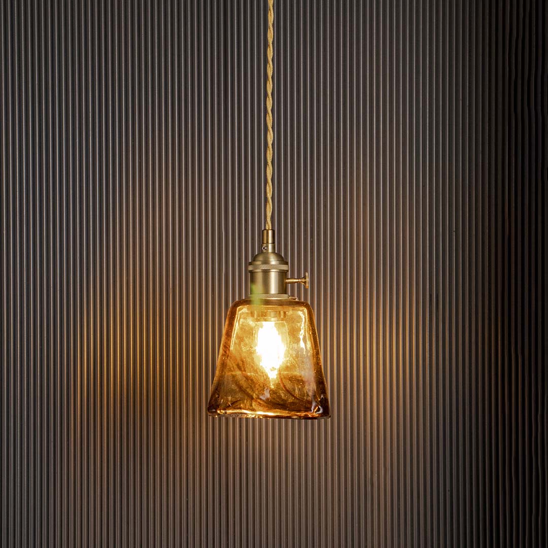 Amber glass pendant light glowing warmly on black background perfect for dining room kitchen and living spaces.