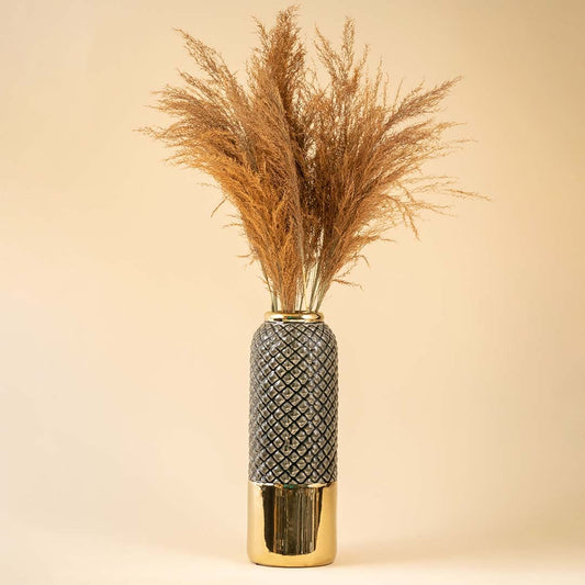 A tall textured grey and gold vase displayed with dried brown pampas on a soft beige background creating a warm lifestyle decor scene filled with natural elegance.