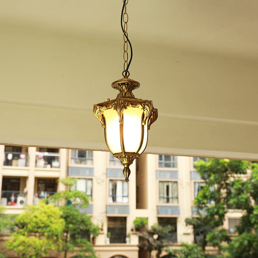 Black metal outdoor pendant light hanging on a porch ceiling with warm light on creating an inviting glow against a blurred building background.