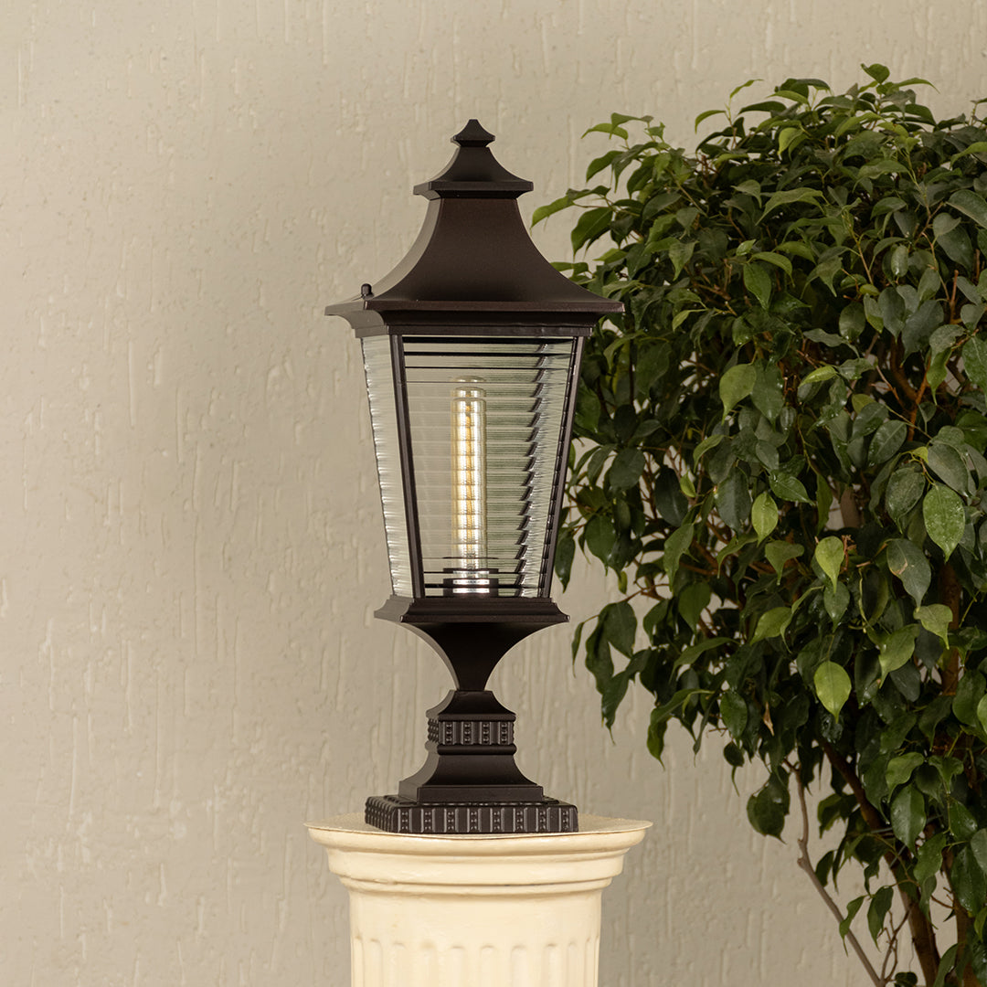 Black metal lantern with ribbed glass Light On placed next to a ficus plant Lifestyle image for patio decor.