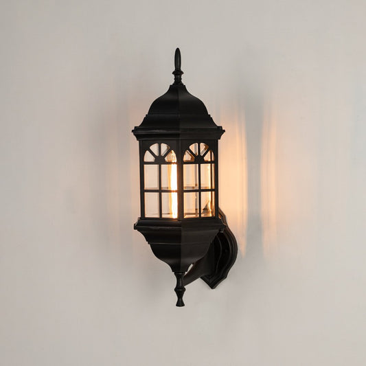 Black metal outdoor wall light on white background with an arched paneled glass shade for vintage patio decor.