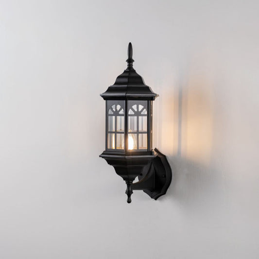 Black metal outdoor wall light on white background with an arched paneled glass shade for vintage patio decor.