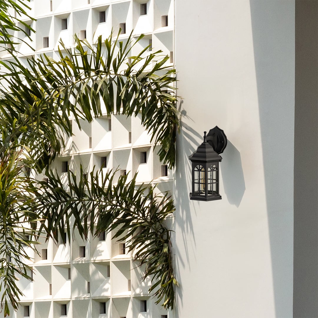Black outdoor lantern with the light off installed on a bright exterior wall highlighting its traditional hexagon frame and arched window style glass design.
