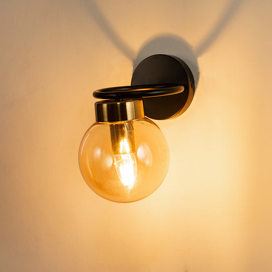 Closeup of amber glass and black metal wall light with warm glow for premium modern decor styling spaces.