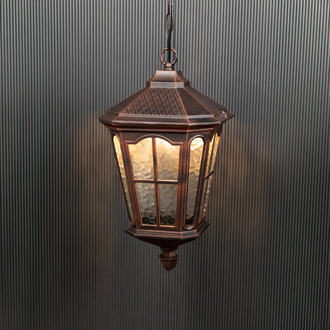 Outdoor hanging lantern glowing warmly against a black background highlights its detailed design.