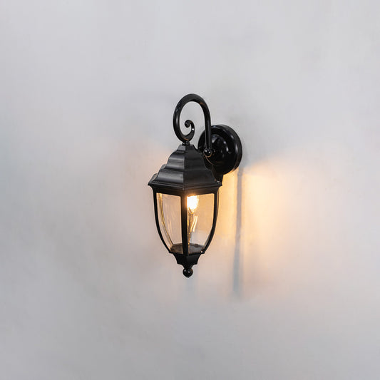 Black metal outdoor wall light on white background with a classic glass lantern shade casting a soft warm glow for decor.