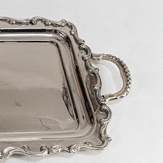 Elegant silver tea set with tray kettle milk and sugar pots placed on a wooden table in a cozy living room with cushions.