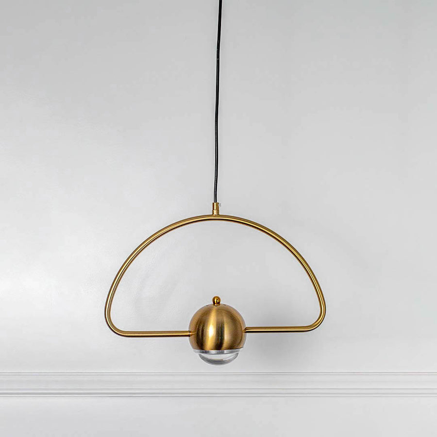 Gold semicircle pendant light with central bulb holder and hanging cord placed against neutral wall background enhancing stylish modern lighting aesthetic.