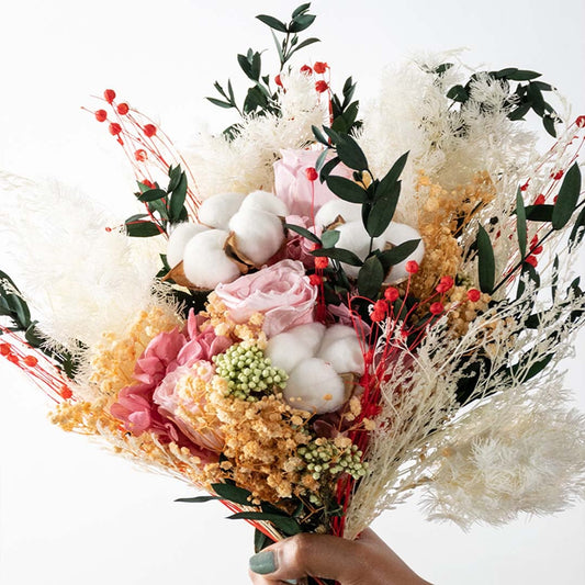 Closeup of artificial flower bouquet with preserved roses cotton stems pampas grass yellow blooms and greenery creating a decorative floral gift.