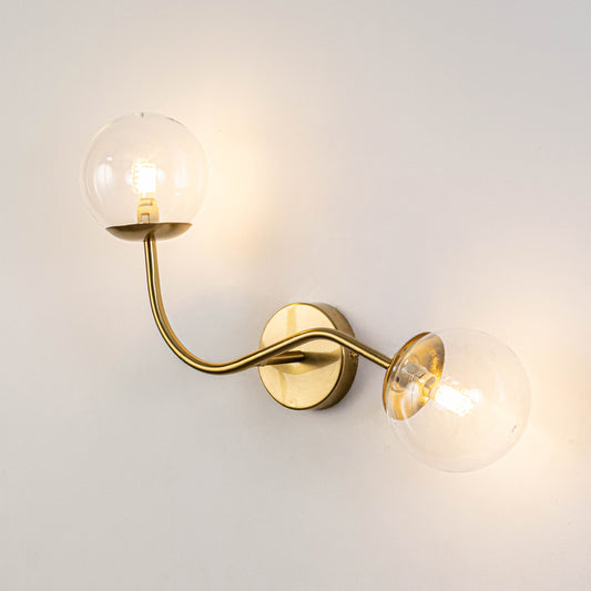 Contemporary dual glass globe wall light with brass metal frame mounted on clean neutral wall background perfect for modern home decor lighting.
