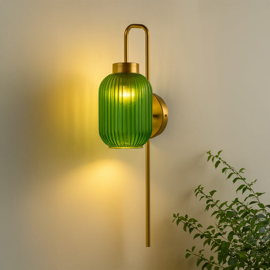Gold metal wall light with green ribbed glass shade emitting warm glow ideal for bedroom or living room wall decor styling.