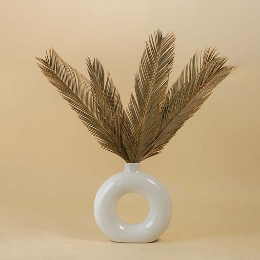 Hand holding golden dried palm leaves against beige background for home decor and floral arrangement styling.