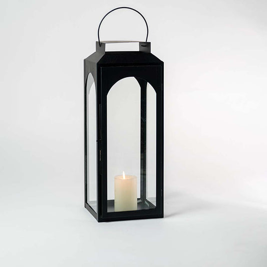 Black lantern with candle lit and glass panels displayed on white background for indoor outdoor styling.