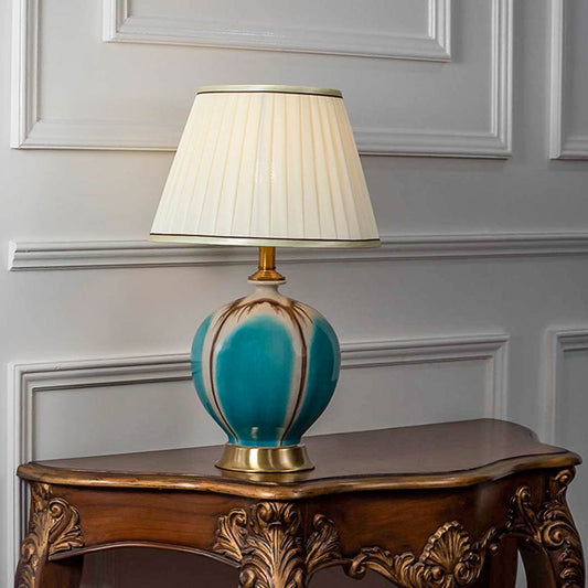 Elegant table lamp with turquoise glass base and pleated white shade on wooden console table ideal for traditional home decor.