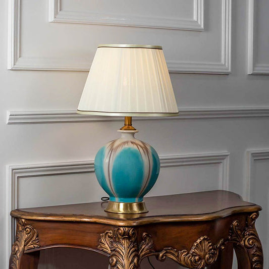 Table lamp with turquoise ceramic base and white fabric shade placed on wooden side table classic decor for living room and bedroom.