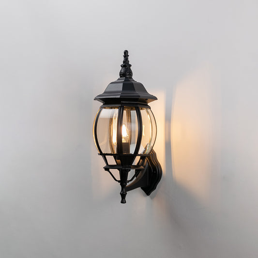 Black metal outdoor lantern wall light on white background with clear ribbed glass for patio decor.