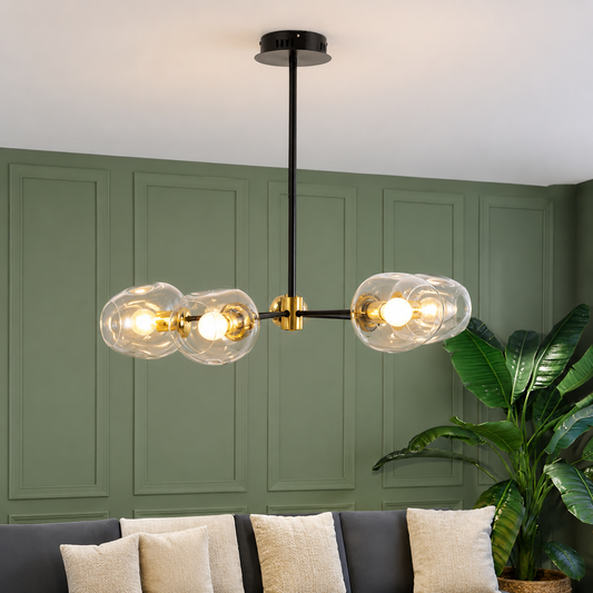 Modern three-light linear chandelier with clear glass bubble shades and gold accents, hanging in a living room with a green paneled wall and sofa.