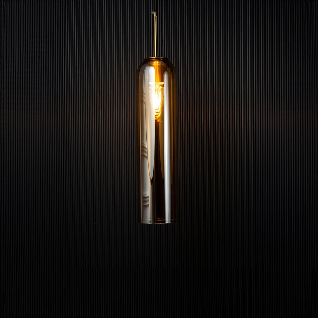 A glowing cylindrical pendant light illuminated against a dark backdrop creating a warm contrast that highlights the shape and reflective glass texture with the light on.