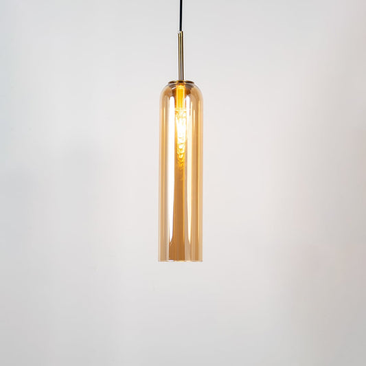 A tall cylindrical pendant light with its bulb glowing warmly on a white background showing its smooth transparent glass body and elegant metal detailing with the light on.