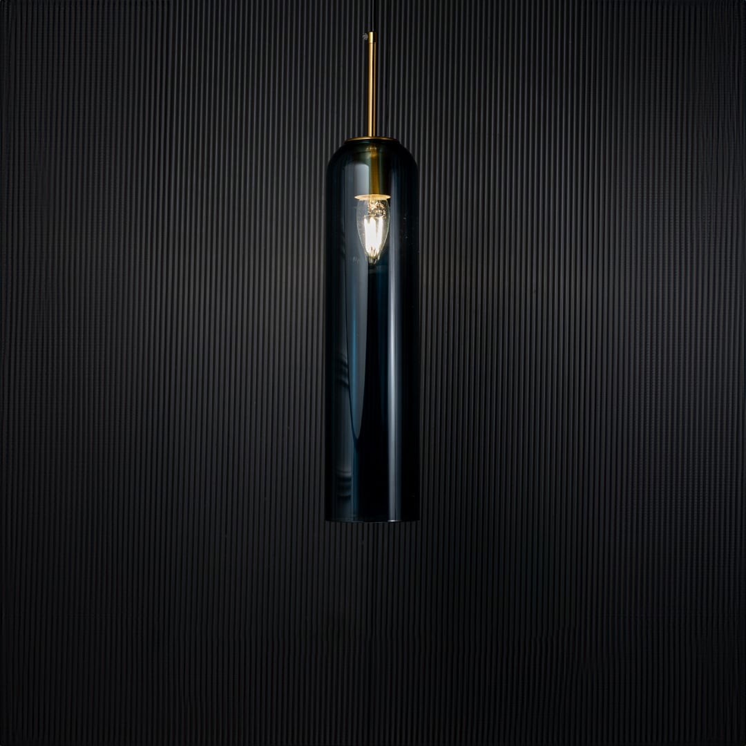 A glowing blue glass pendant light turned on against a deep black background creating a striking contrast that enhances its tall transparent design and warm radiance.