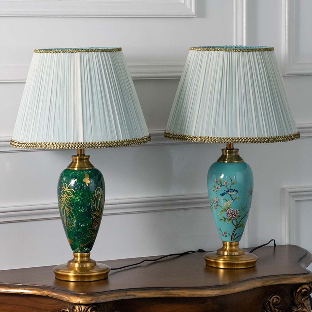 Emerald green ceramic table lamp featuring intricate gold leaf detailing and a pleated white shade turned off on a white background highlighting its glossy artistic finish.