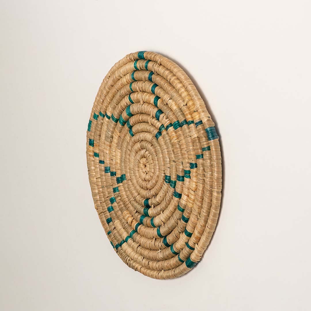 Side profile of the flat woven wall basket showing the thick natural fiber coils and teal stitching details on a white surface.