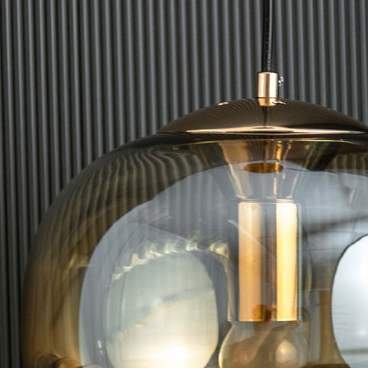Closeup of smoke glass and brass metal pendant light showcasing reflective finish and craftsmanship.