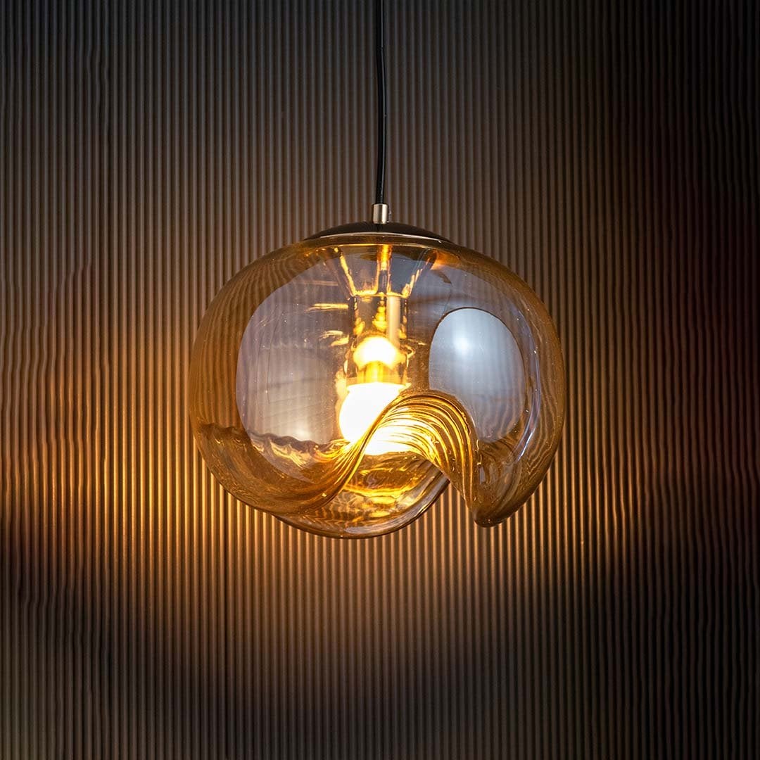 Artistic curved glass pendant light glowing softly with warm light highlighting its wave design and golden core against a deep black background.