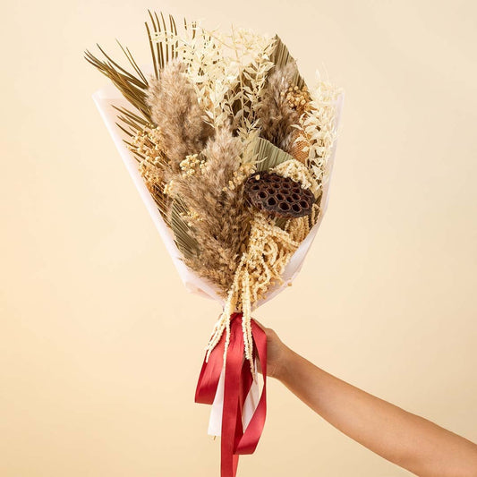 Rustic dried flower bouquet with pampas palm leaves ruscus and lotus pod wrapped with red ribbon on plain background.