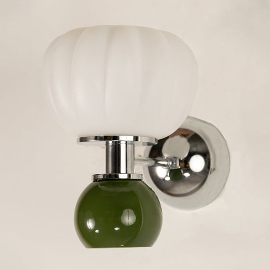 Close up view of polished chrome metal arm connecting the ribbed white glass shade and glossy green glass globe of the wall light.