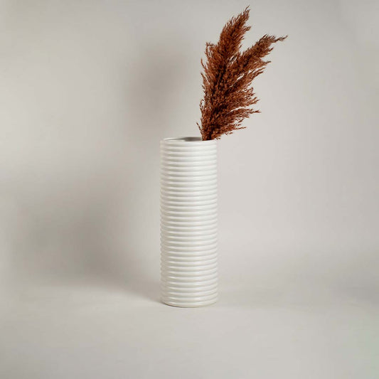 Glossy white cylindrical ceramic vase with linear ribbed design on white background reflecting minimal modern decor.