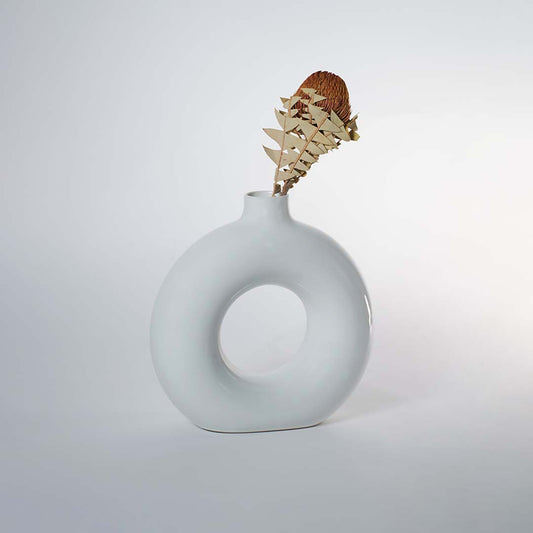 A glossy white circular vase on a white background showing its smooth rounded shape with a central hollow design that highlights its modern sculptural style.