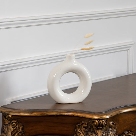 Modern ceramic donut vase in glossy white finish displayed on wooden table with wall paneling elegant lifestyle home decor.