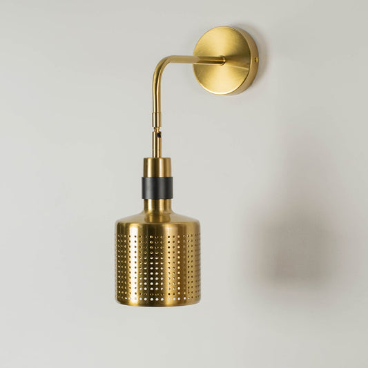 Gold wall mounted light with a perforated shade and black accent displayed without light against a white background focusing on its elegant design.