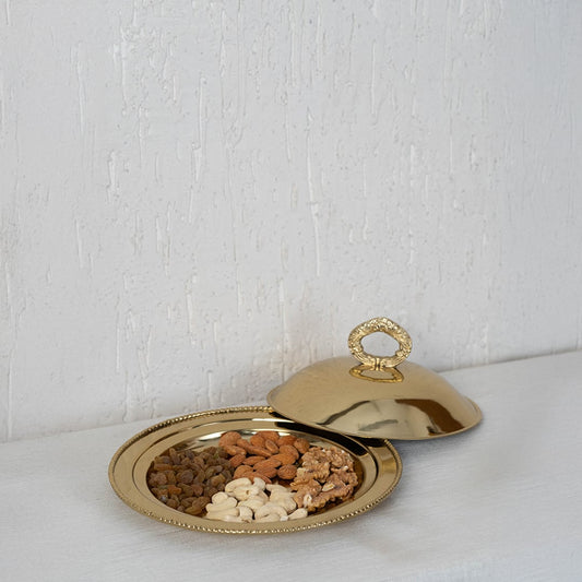 Main product image of gold-tone serving platter with dome lid and ring handle highlighting curved form and polished finish.