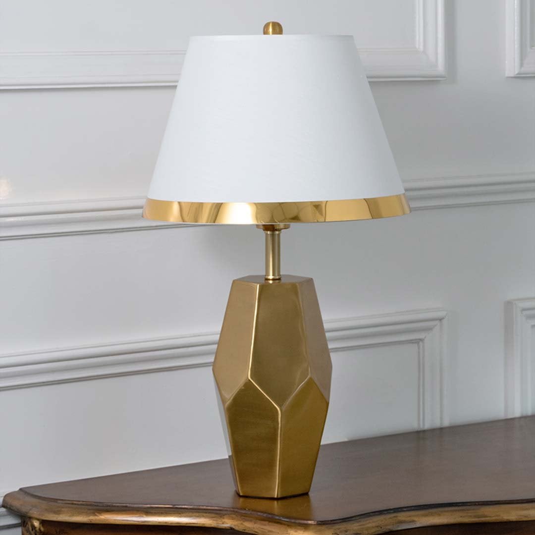 Gold faceted table lamp with white tapered shade and modern sculpted base displayed on a white background perfect for elegant interior styling.